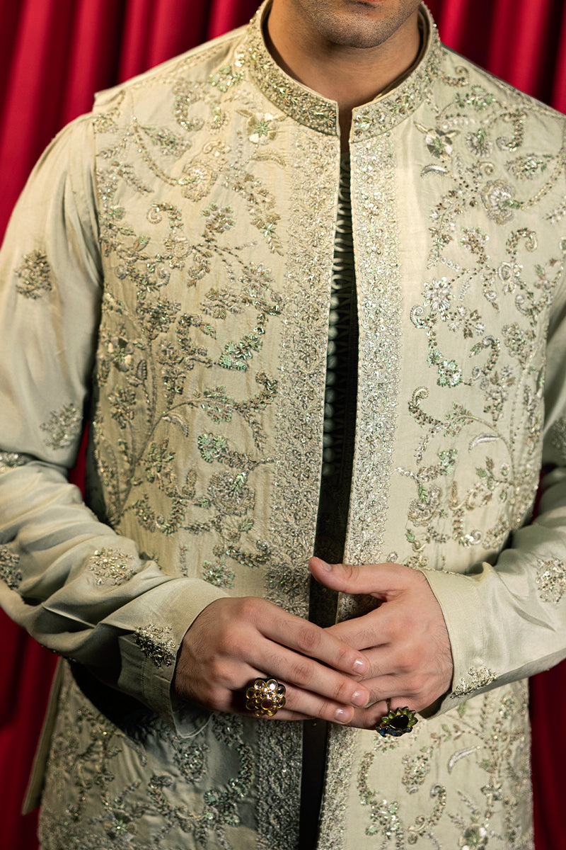 A pastel green waistcoat made from luxurious silk, intricately hand-embellished with Mughal floral patterns using matte sequins, tilla, resham, and cut dana thread-work. It is paired with a matching kurta and pajama set featuring a detailed floral neckline with an all-over motif, enhanced with sequins and resham embroidery.