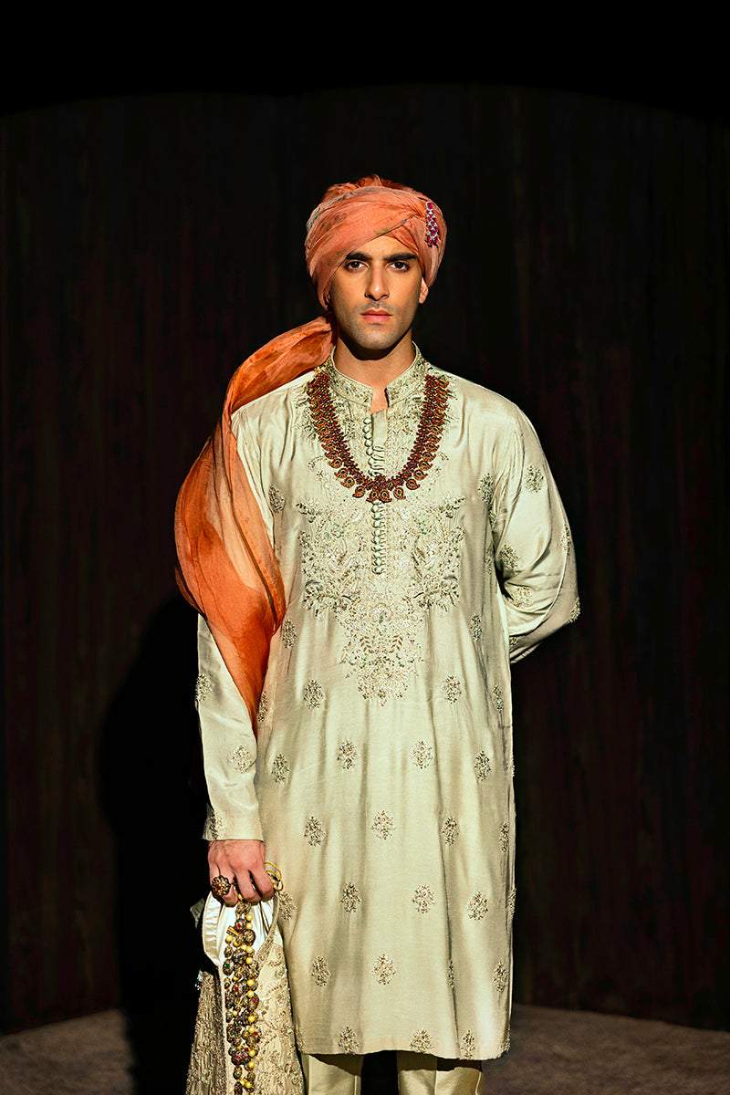 A pastel green waistcoat made from luxurious silk, intricately hand-embellished with Mughal floral patterns using matte sequins, tilla, resham, and cut dana thread-work. It is paired with a matching kurta and pajama set featuring a detailed floral neckline with an all-over motif, enhanced with sequins and resham embroidery.