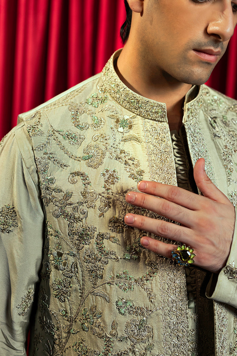 A pastel green waistcoat made from luxurious silk, intricately hand-embellished with Mughal floral patterns using matte sequins, tilla, resham, and cut dana thread-work. It is paired with a matching kurta and pajama set featuring a detailed floral neckline with an all-over motif, enhanced with sequins and resham embroidery.